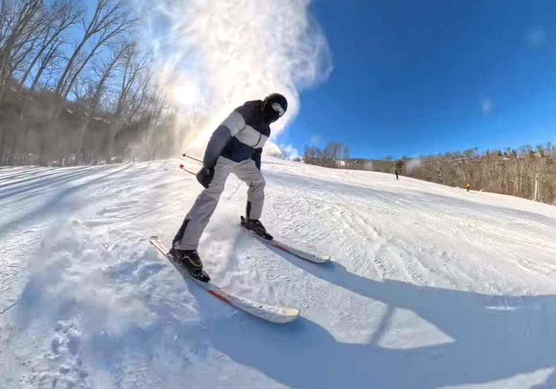Arjun skiing down a bright snowy slope beneath a clear blue sky.